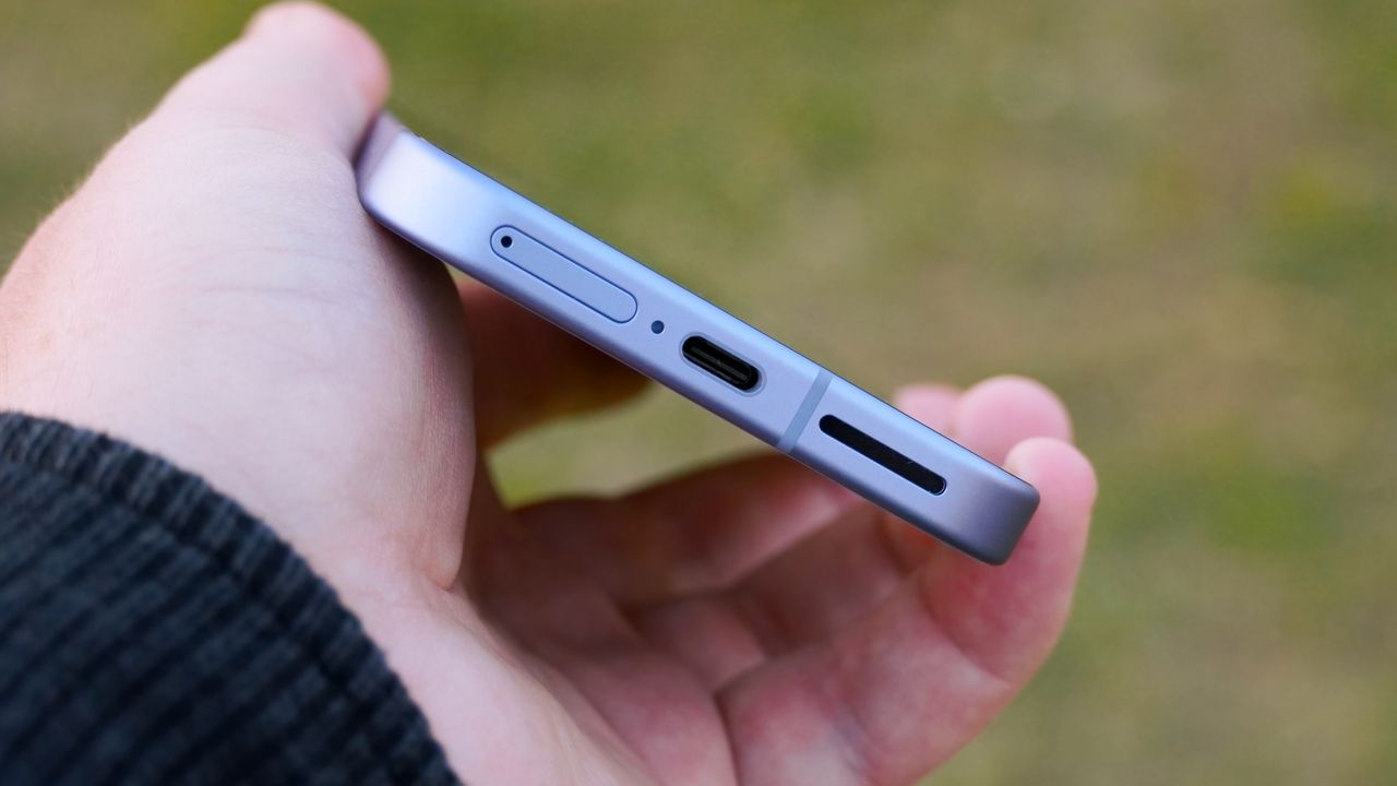 The Google Pixel 9a in the hand showing the USB-C port and SIM tray.