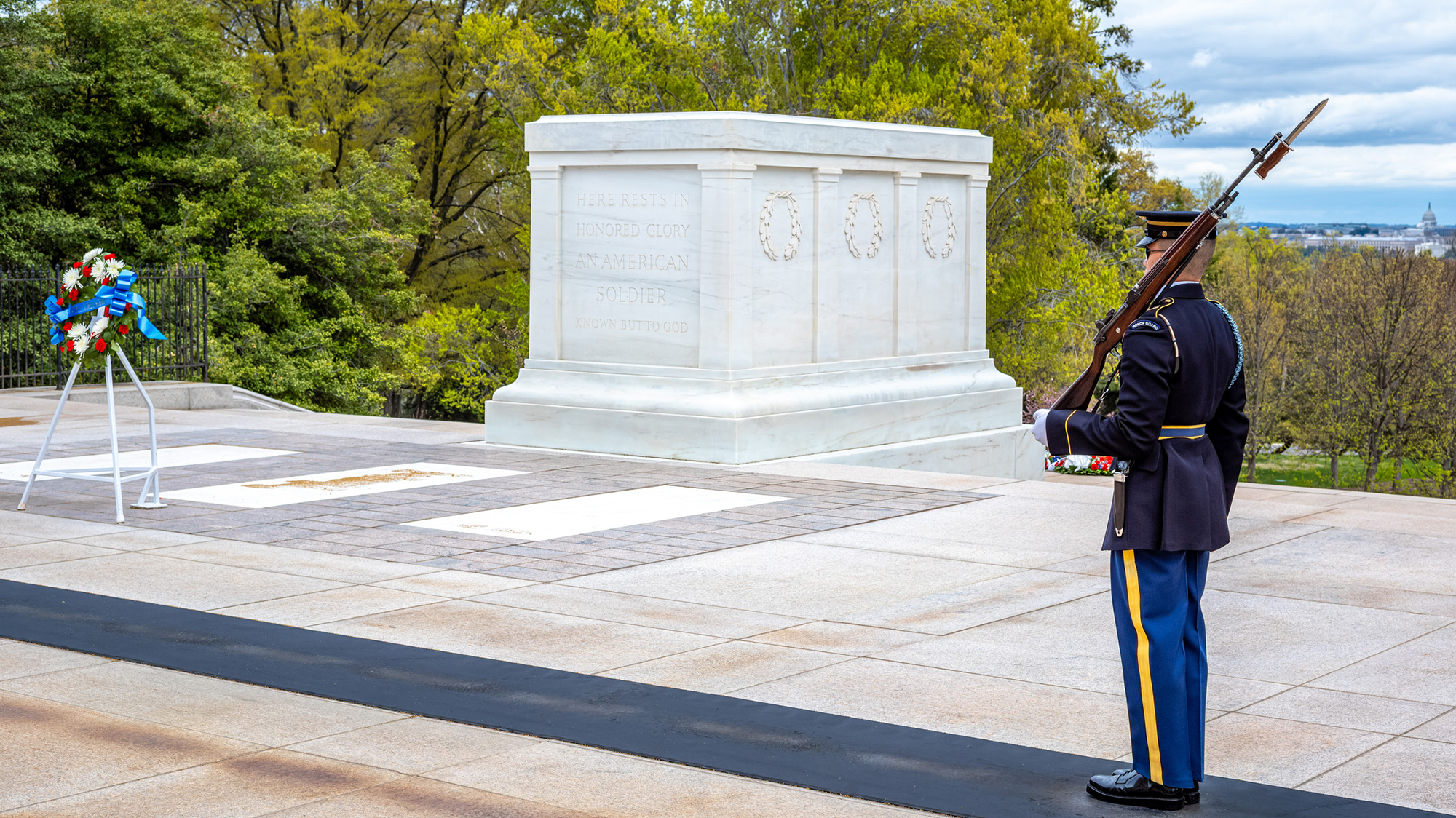 A man in uniform with a gun over his left shoulder stands in the middle of a large monument.