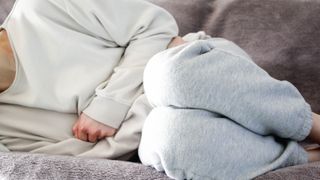 a photo of a woman laying on the couch and clutching her stomach in pain