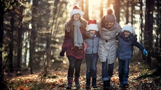 Mother and kids enjoying walk in forest wearing santa hats