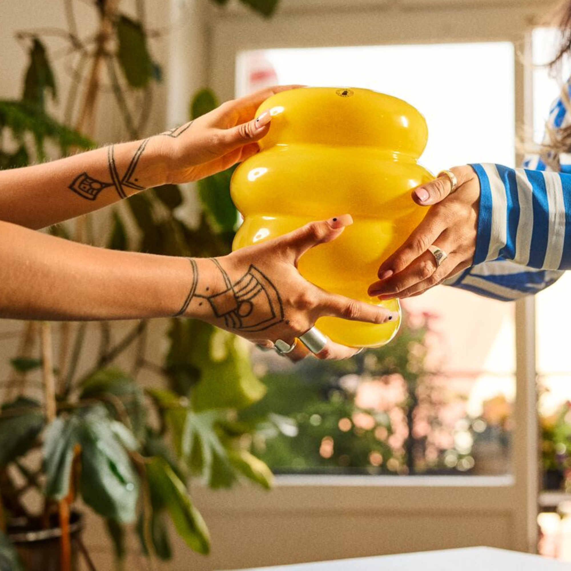 Two sets of hands exchanging a yellow vase.