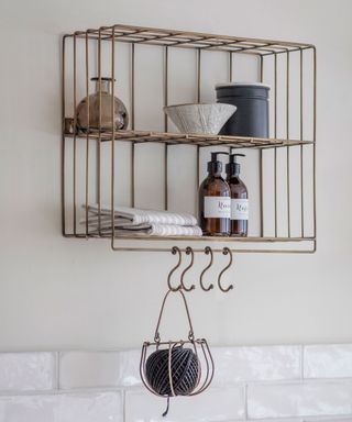 Garden Trading Brompton brass wall rack with various accessories for laundry room on cream wall with white tiles