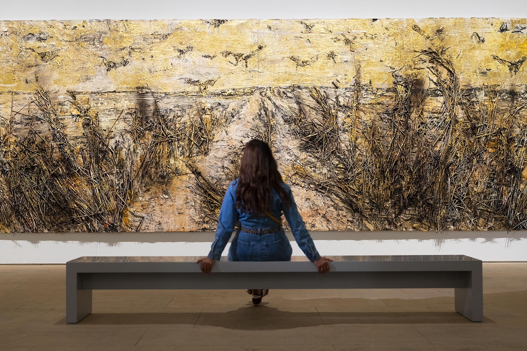person on bench in gallery, looking at large textured painting
