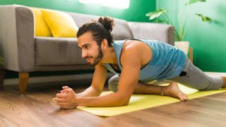 man practicing a pigeon pose on an exercise mat in his living room