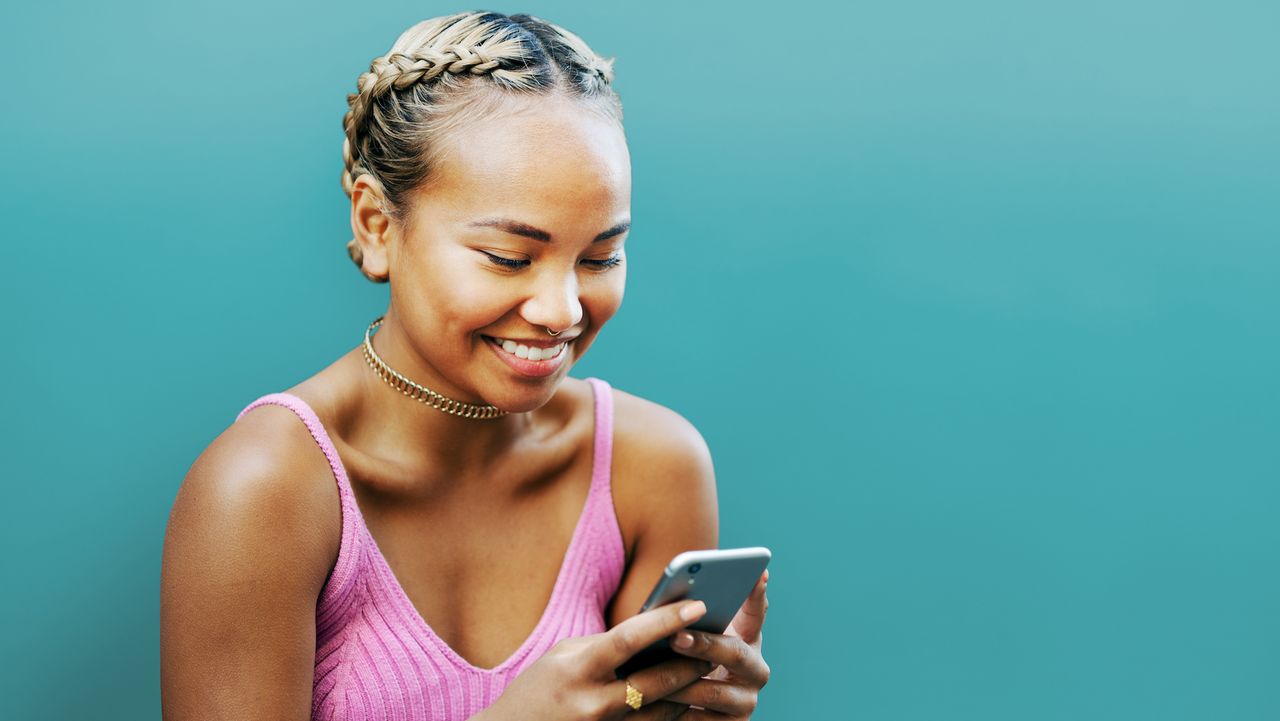 Woman smiling with smart phone, blue wall - stock photo