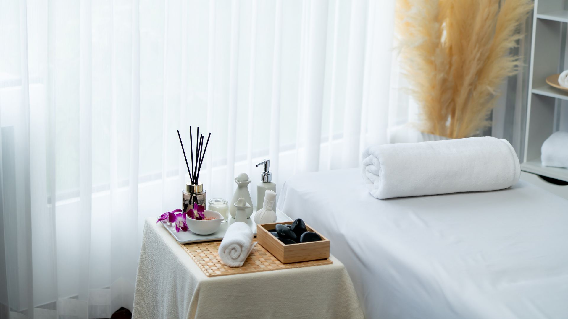 A tranquil reflexology room with bed, reed diffusers, and clean white towels.