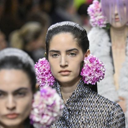 Models on a runway. Each has oversized pink and white flower earrings