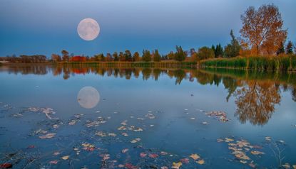 november 2022 full moon; a full moon over a lake with autumn trees in the background