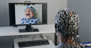 African woman with electrical nodes attached all over her head looking at a screen with a baby crying on it.
