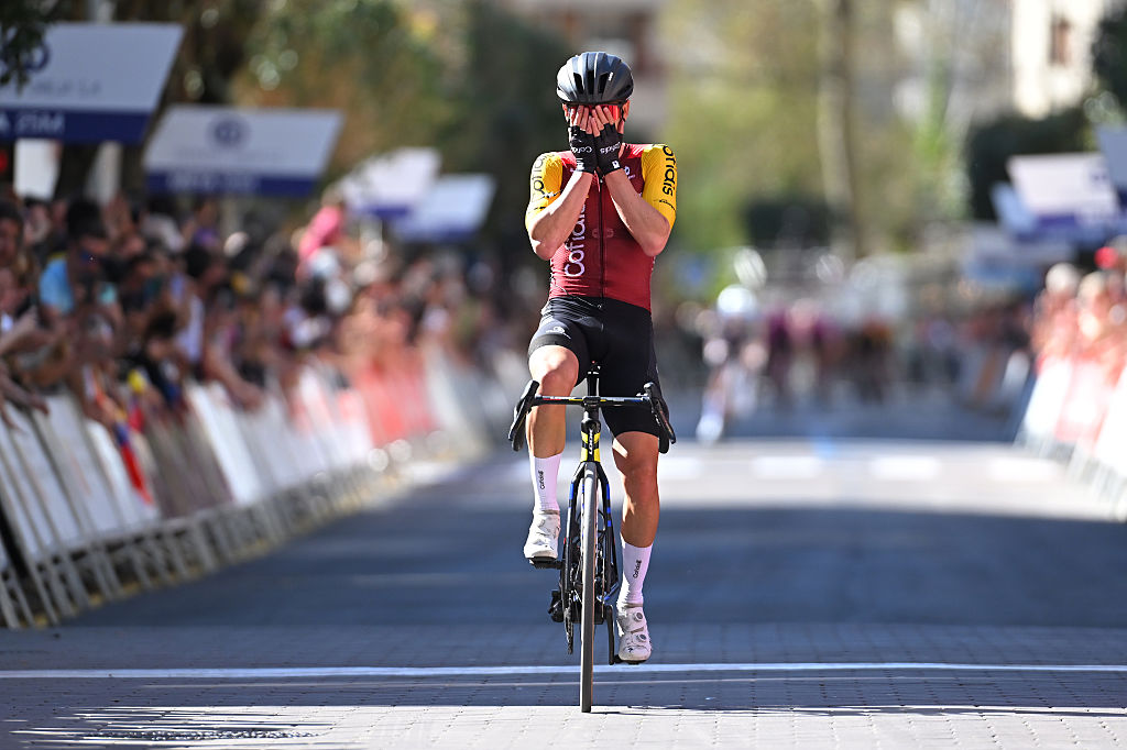 Ion Izagirre puts his hands over his face in disbelief at the finish line with Simmons in the distance