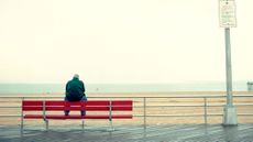 A man sits on a bench overlooking a forlorn-looking beach and the ocean.