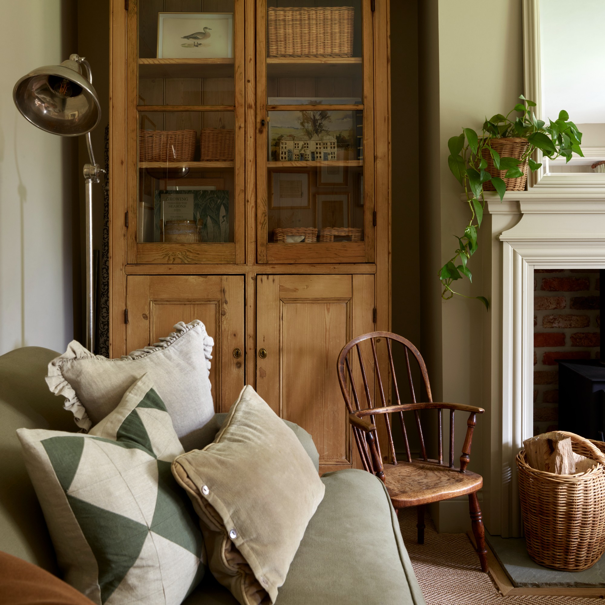 A neutral rustic living room with a vintage display cabinet and a green sofa with mismatched cushions