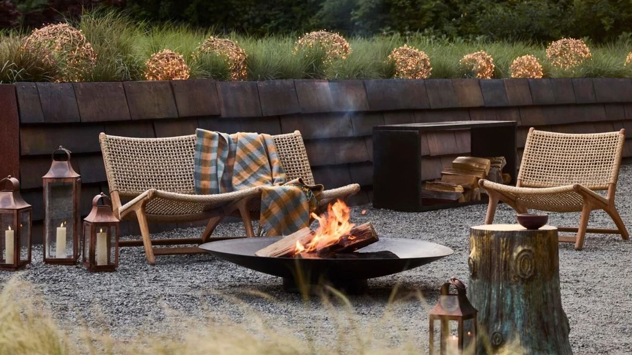 shingle outdoor sunken patio area with wicker and wood furniture, a firepit, lanterns, and a plaid blanket