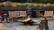 shingle outdoor sunken patio area with wicker and wood furniture, a firepit, lanterns, and a plaid blanket