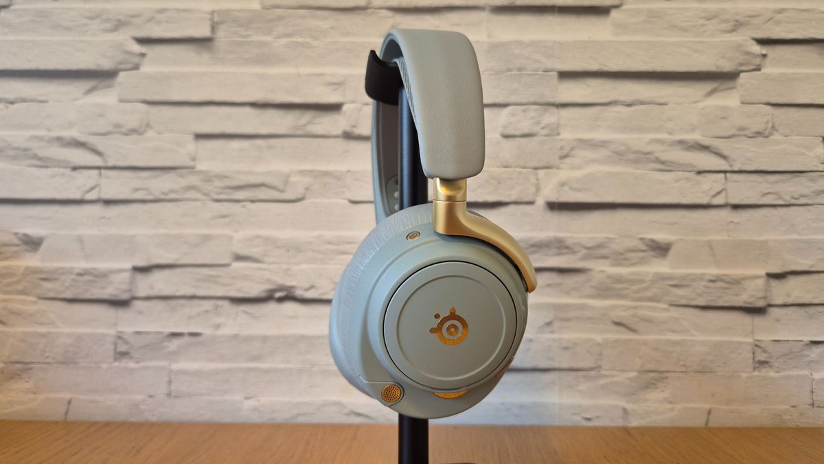 The SteelSeries Arctis Nova Elite headset in front of a white brick background and on a wooden surface