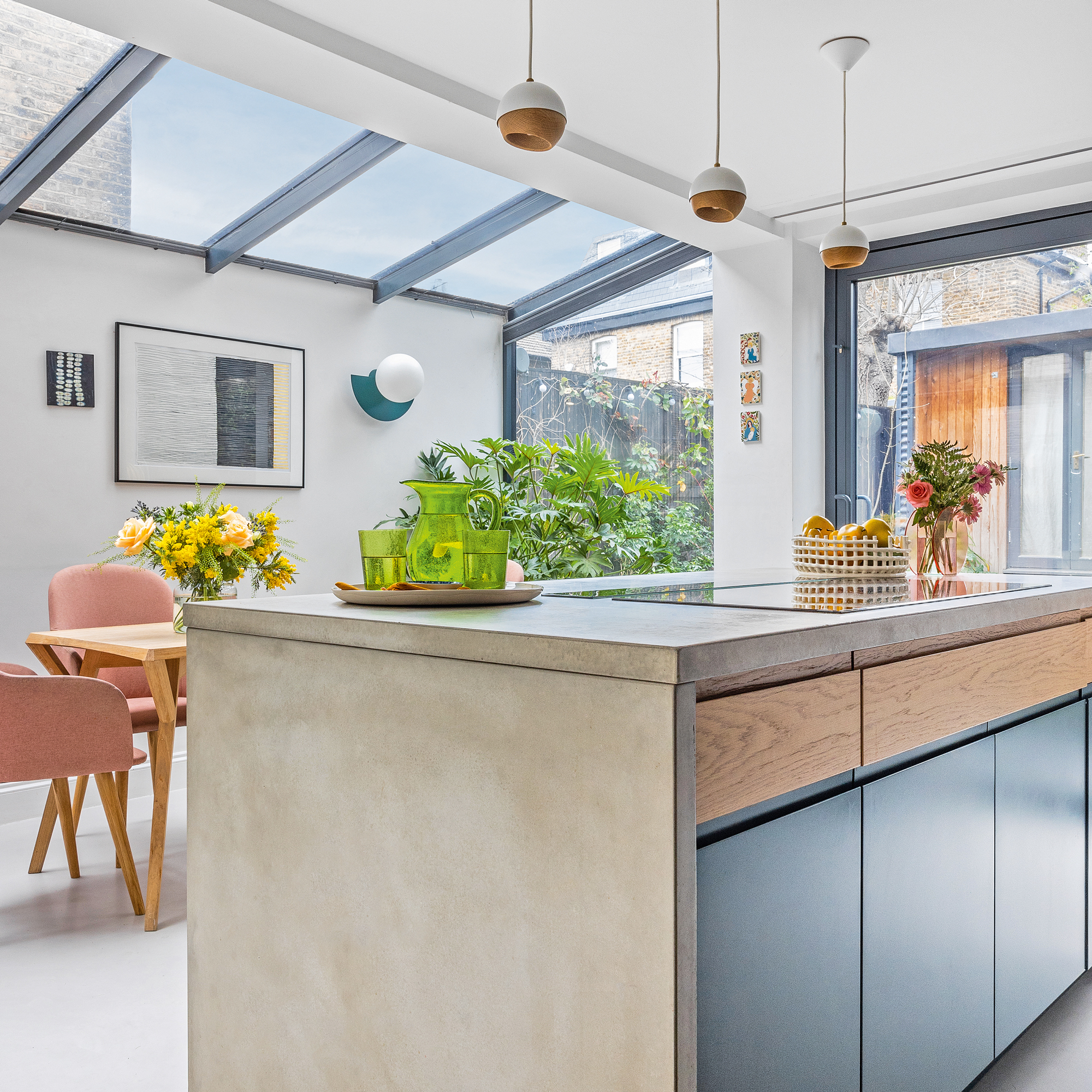 an open plan kitchen diner with side return extension with dark blue cabinetry and pink upholstered dining chairs