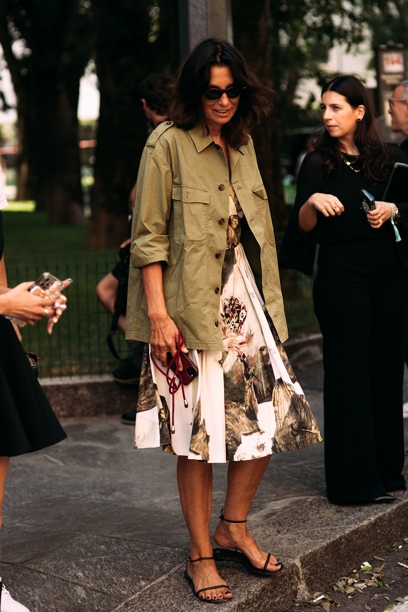 fashion week attendee wearing sunglasses, green jacket, floral dress, and black sandals