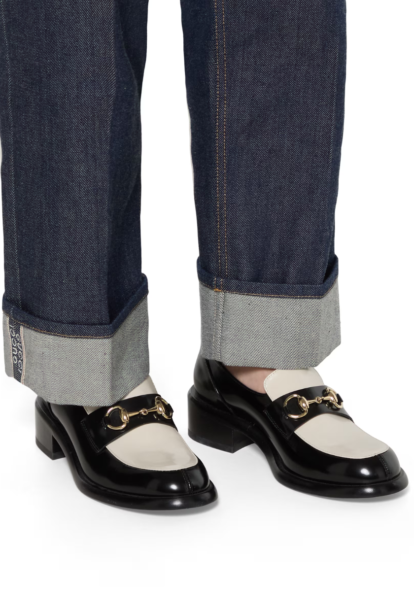 A pair of black and white Gucci loafers with a horsebit detail. 