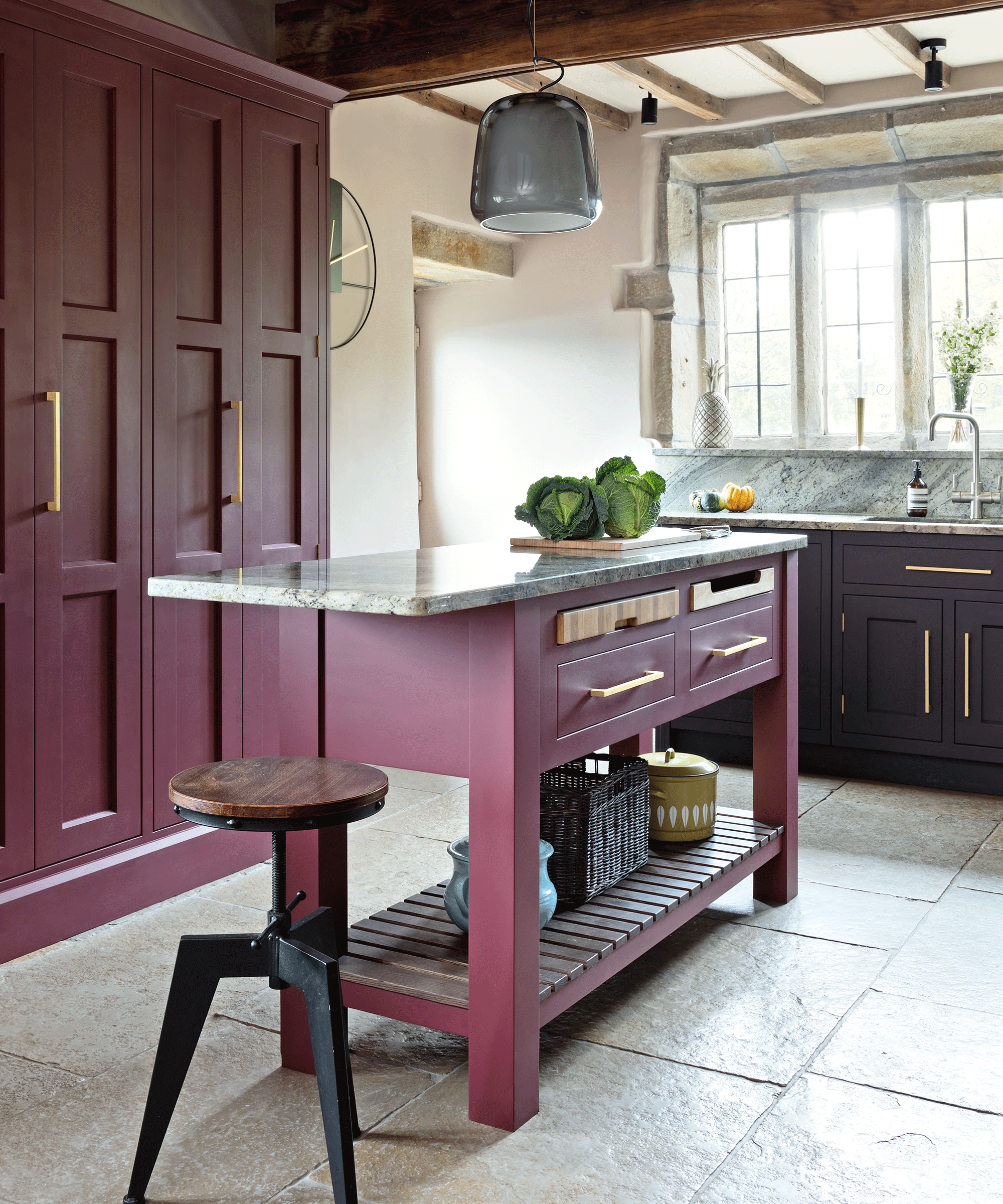 A burgundy freestanding kitchen island with a marble top and an industrial style bar stool
