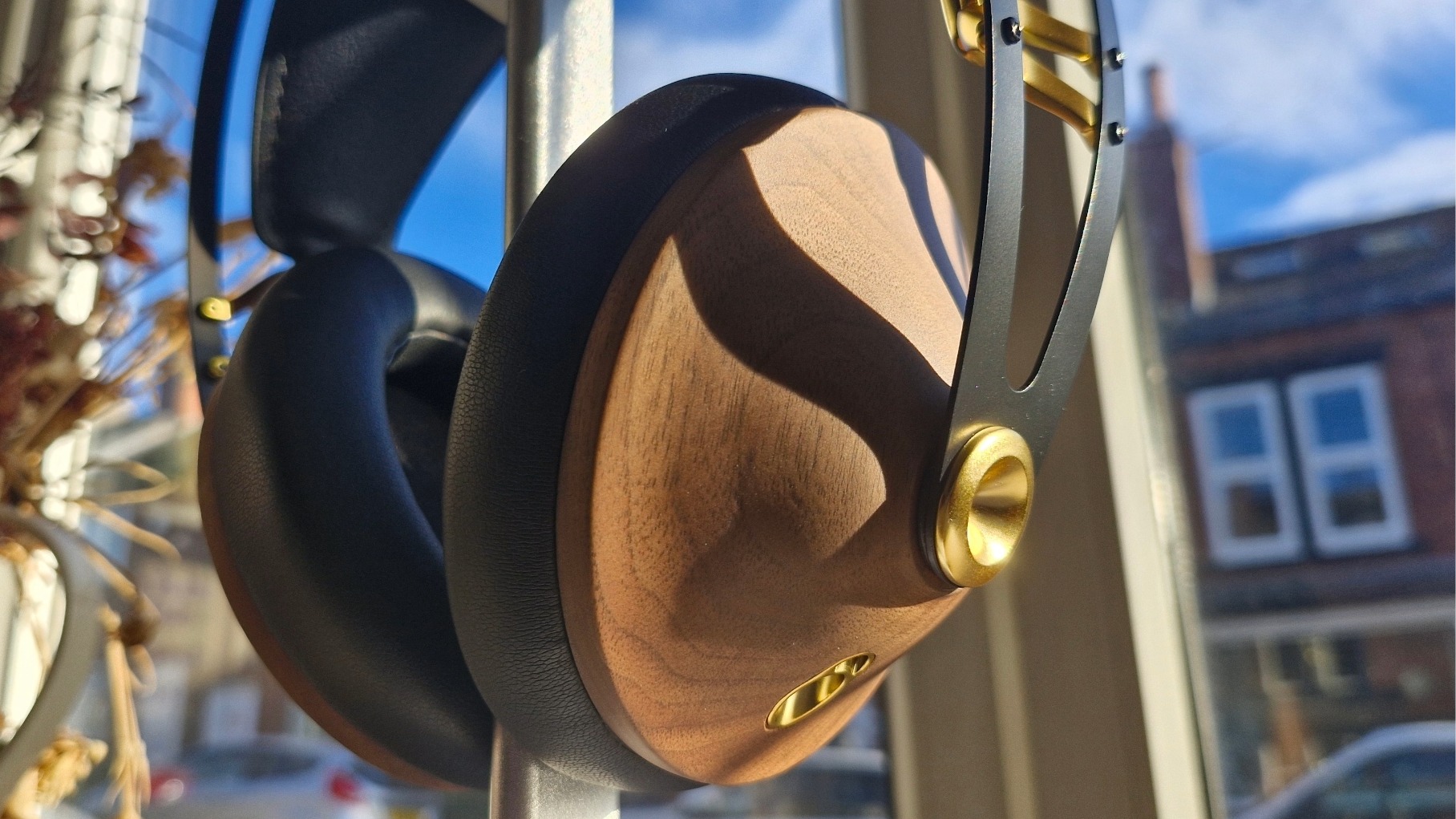 Closeup of the walnut earcups of the Meze Audio 99 Classics 2nd Gen over-ear headphones, on a headphone stand.