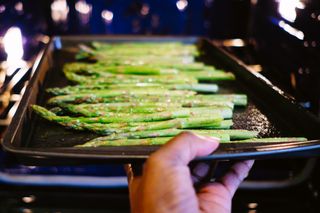 Asparagus on a roasting tray being put in the oven
