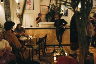 A candle-lit modern industrial bar features tiled terracotta and white floors, bistro-style furniture, and plants.