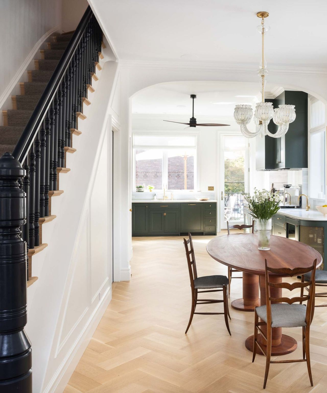 A brownstone living room with an arched doorway, dining space, green kitchen, and dark stairway