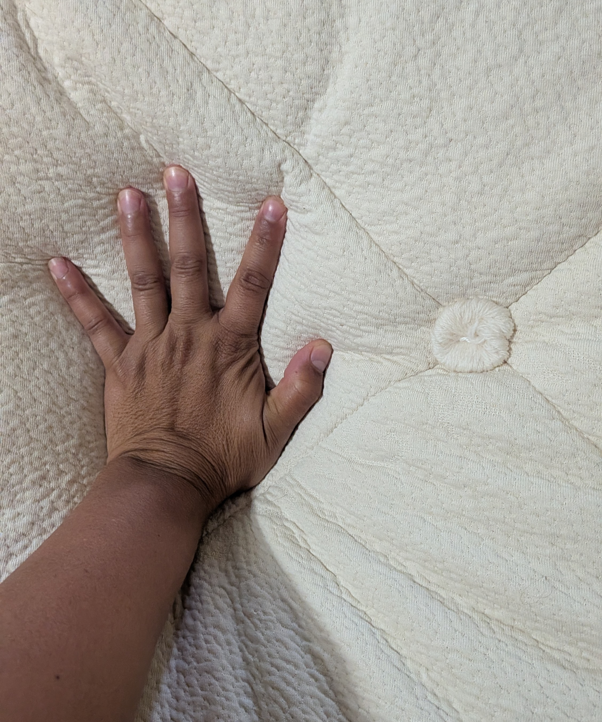 A hand pressing into the surface of the Avocado Luxury Organic Mattress.