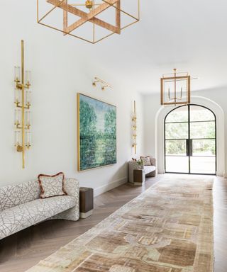 white foyer with gold lanterns, gold wall sconces, geometic sofas, patterned rug and green and blue artwork