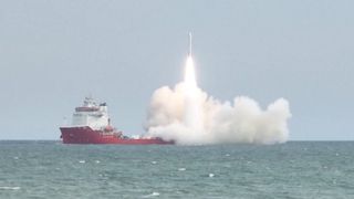 a rocket launches from a red ship at sea.