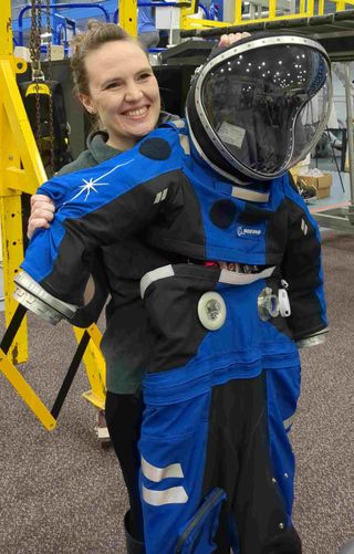a woman holding up a spacesuit and smiling