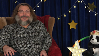 Jack Black with a huge beard sitting in an armchair next to a toy panda for "CBeebies Bedtime Stories"