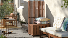 IKEA Namarro Privacy Screen and Garden Box - a light brown wood stained slatted privacy screen with a garden storage box with two cushions on top, next to an outdoor sofa and separate privacy screen in an outdoor living area