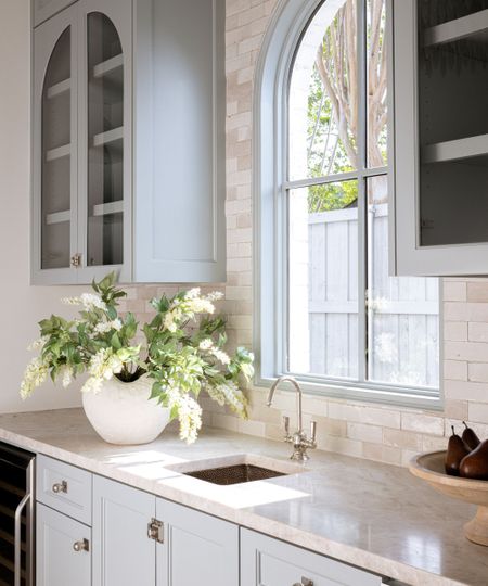 Kitchen with granite countertops, Boothbay Gray painted cabinetry, a ceramic white vase with white flowers, and an arched window with grey painted frame