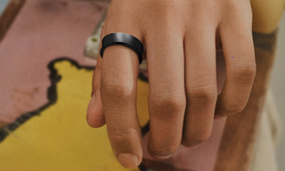 The Titanium Black Samsung Galaxy Ring on the finger of a person who is holding a skateboard.