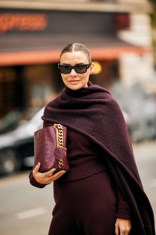 A woman in a burgundy sweater, skirt, scarf and red bag