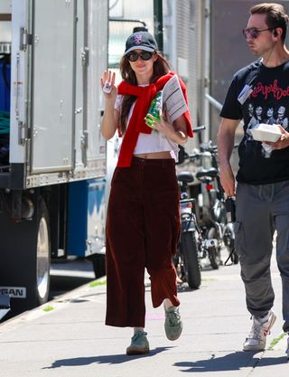 Dakota Johnson wearing t-shirt, brown pants, red scarf, and green Adidas Sambas.