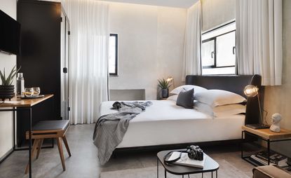 Bedroom with white linen and dark wood headboard and cupboards, small desk and stool for seating with side tables and lamps