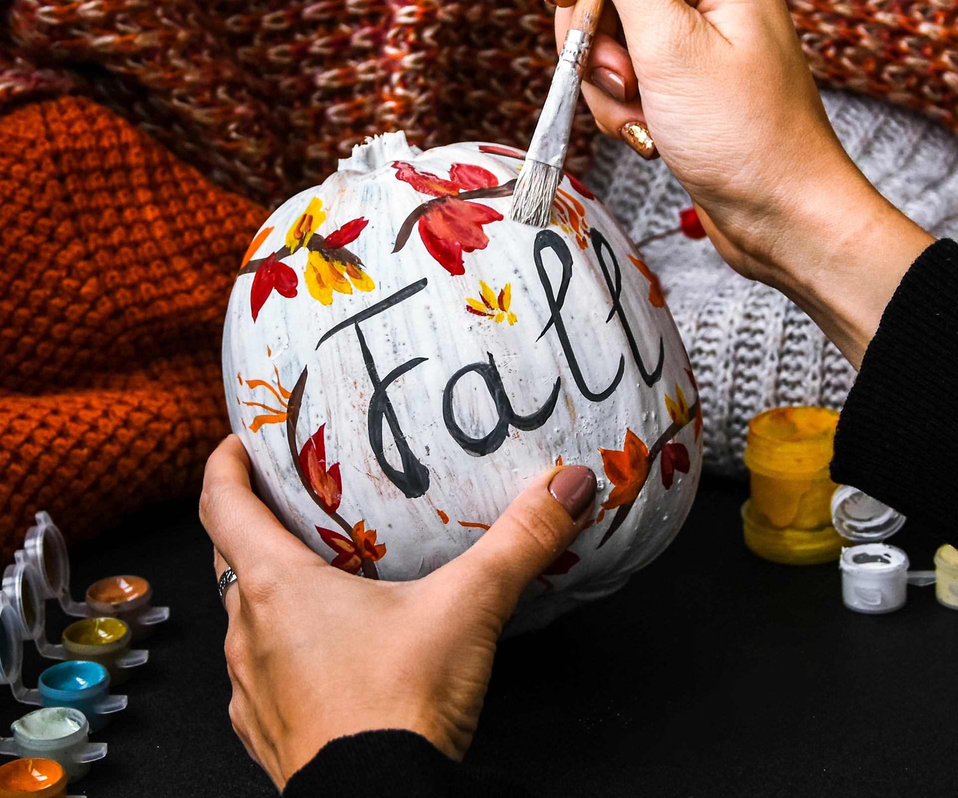 DIY. Do it yourself. Woman paints thanksgiving decorations on orange pumpkin for Halloween. Autumn harvest. Sweater home cozy. Paintbrush