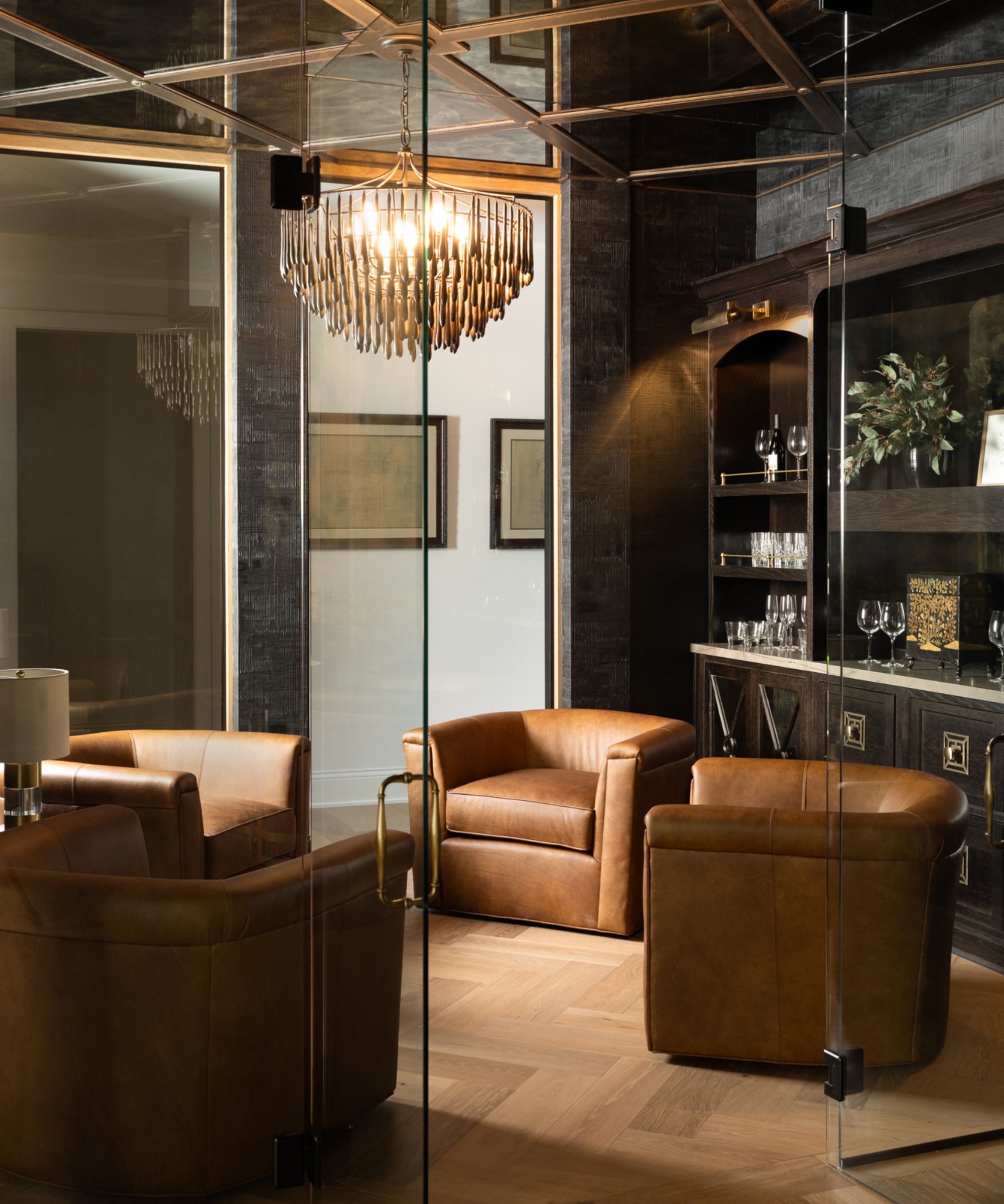 Wine cellar in a basement, with glass doors and four brown leather chairs.