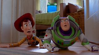 Woody and Buzz Lightyear looking at each other while crawling on the floor with Lilypad behind them