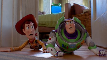 Woody and Buzz Lightyear looking at each other while crawling on the floor with Lilypad behind them