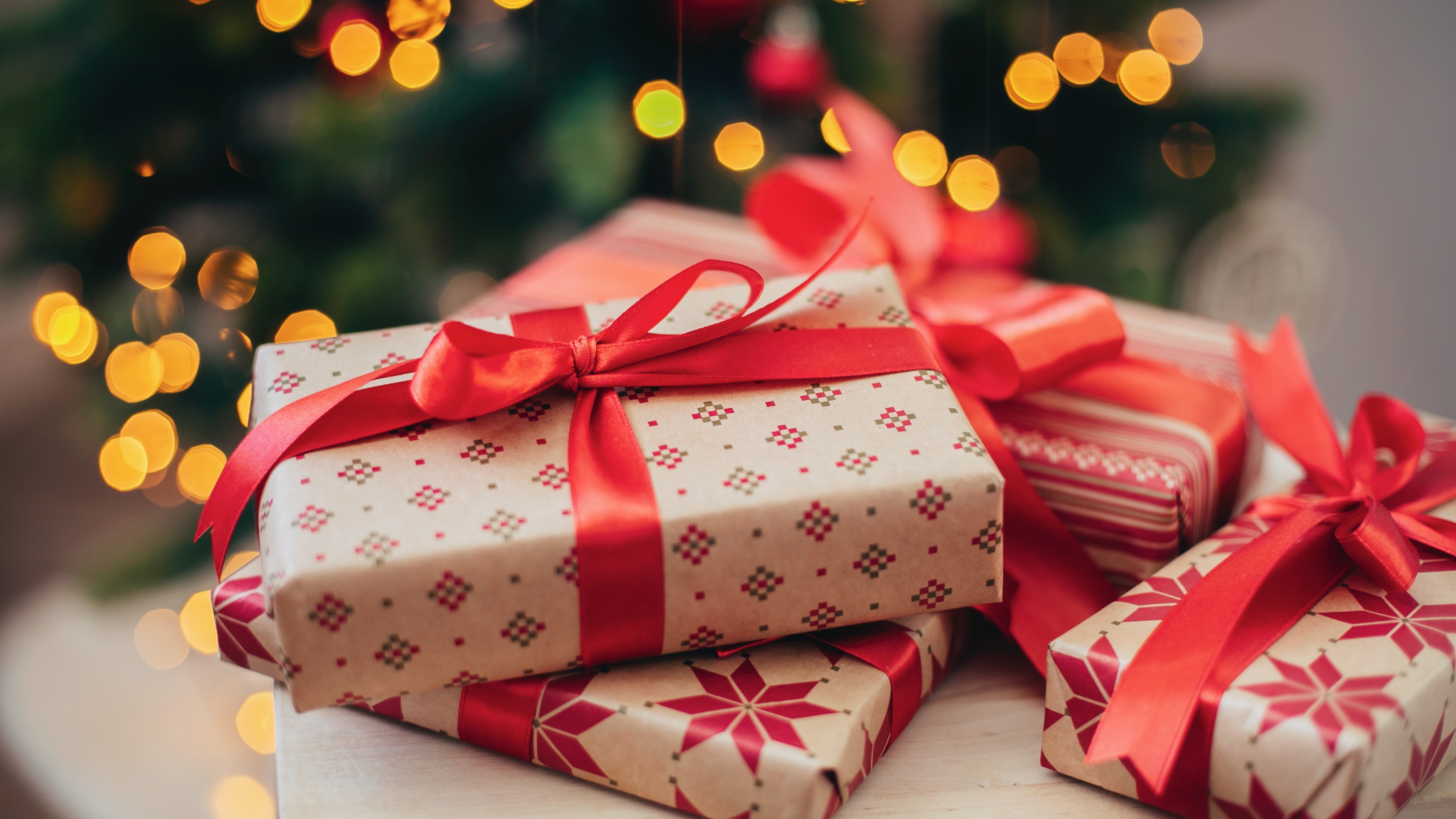 Wrapped Christmas gifts with a lit tree in the background