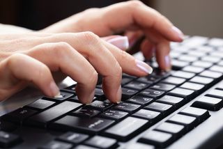 A woman's hands typing on a keyboard.