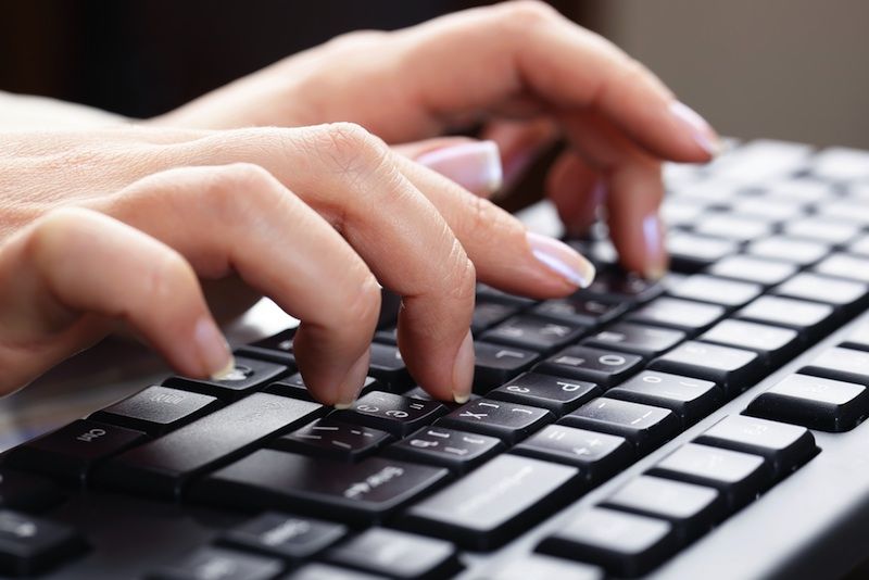 A woman&#039;s hands typing on a keyboard.