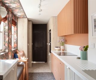 narrow kitchen with built in seating underneath windows, wall cabinets, long white worktop with cabinets below and floor to ceiling cabinets at end of room