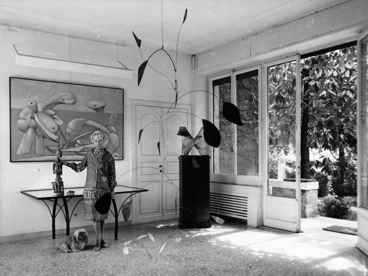 American art collector and millionairess Peggy Guggenheim (1898-1979) in the entrance hall of her eighteenth century Venetian palace. Hanging from the ceiling is a 1941 Alexander Calder mobile and behind her is Picasso&#039;s &#039;On The Beach&#039;.