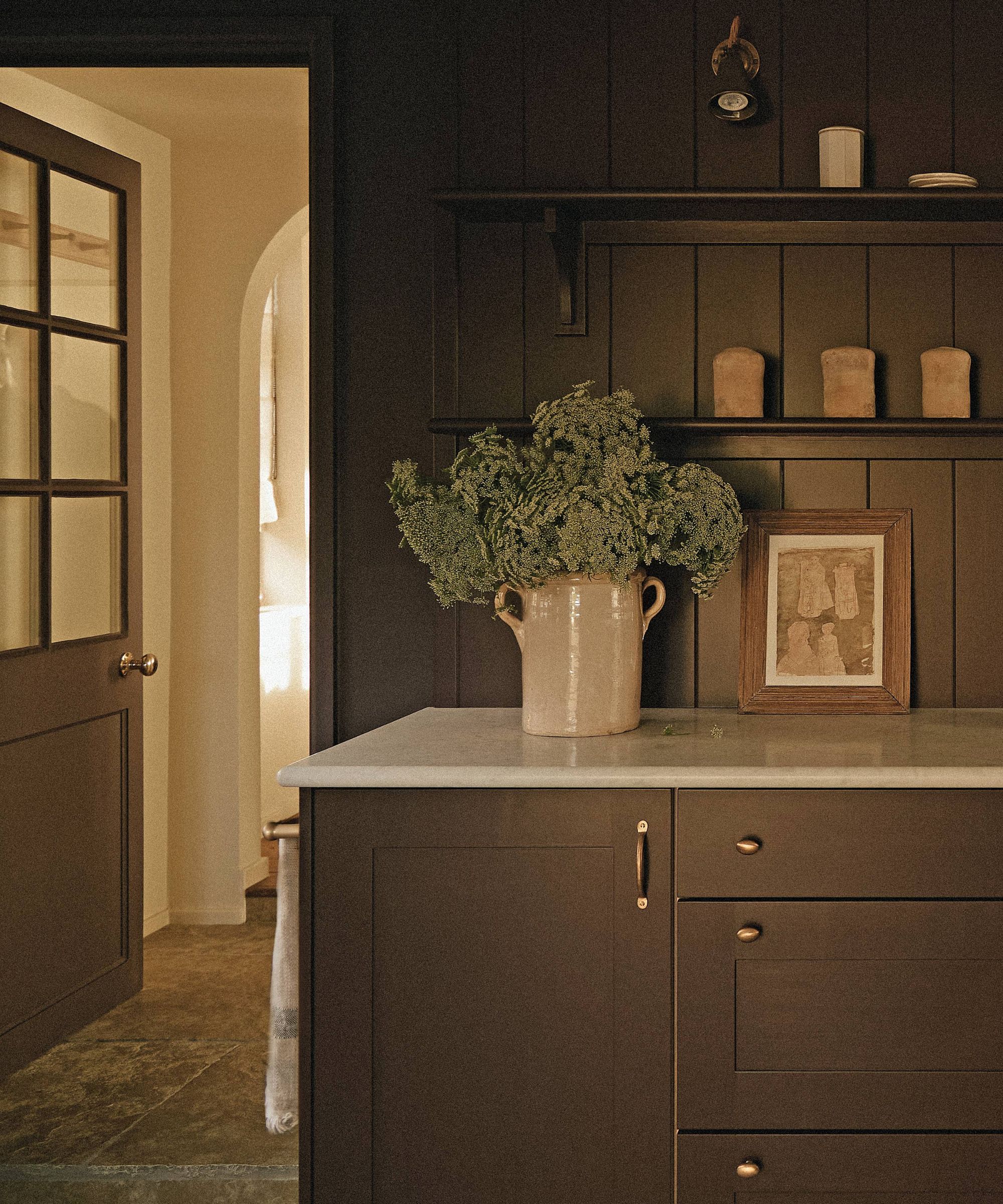 a dark moody boot room with paneled walls, painted cabinetry and flagstone floors