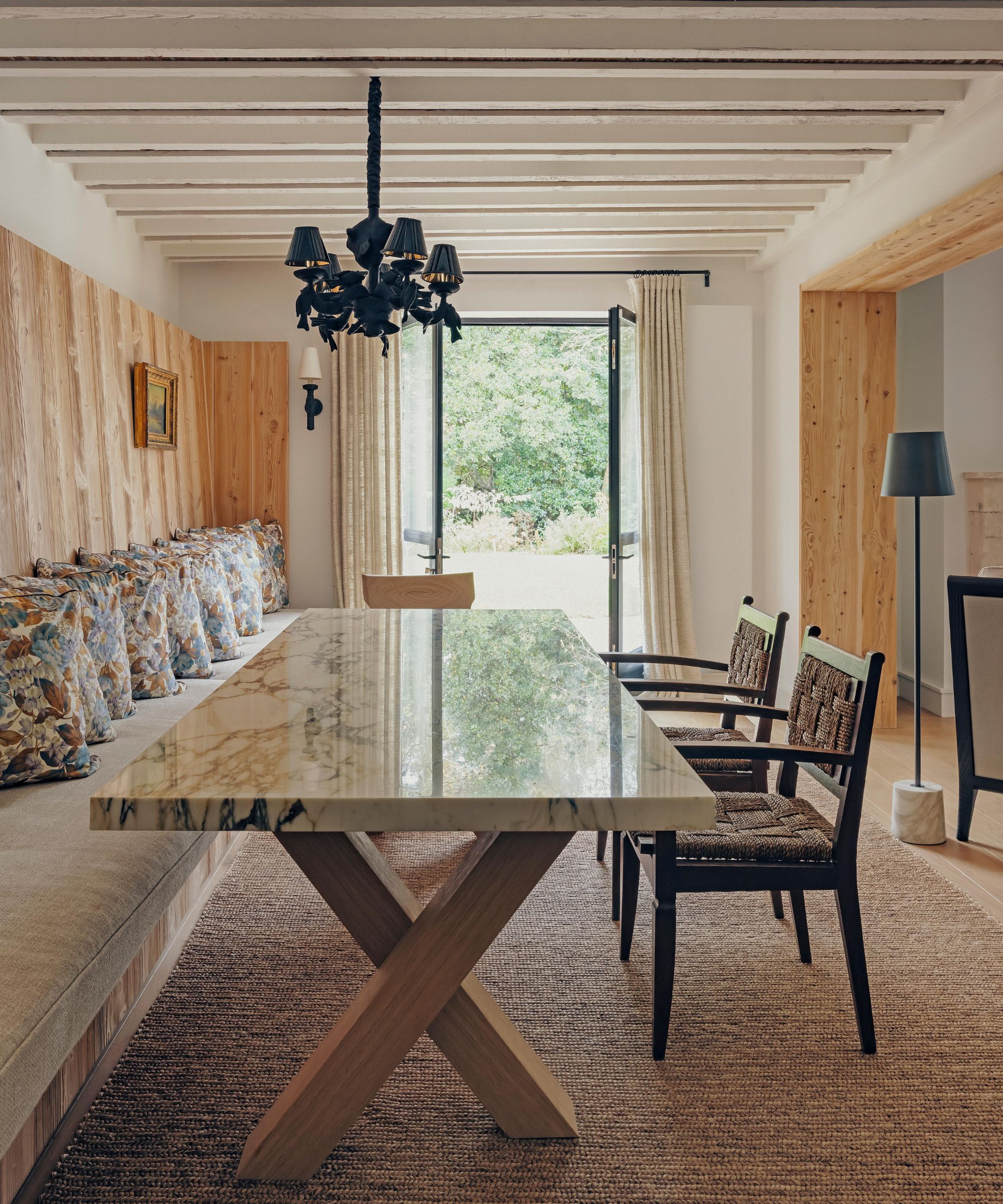 a wood clad dining area with rustic ceiling beams, a marble table, banquette seat and rattan chairs