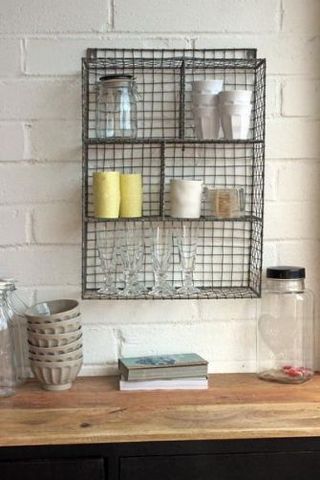 A wire mesh shelving unit mounted to a white brick wall in a kitchen.